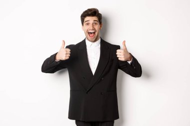 Yeni yıl partisi, kutlama ve yaşam tarzı kavramı. Siyah takım elbiseli, afili ve memnun yakışıklı bir adamın portresi, ürün gibi, güzel, beyaz bir arka planı onaylıyor.