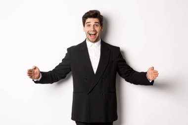 Heyecanlı takım elbiseli yakışıklı bir adamın portresi, fotokopi alanında büyük bir nesne şekillendiriyor ve hayret içinde gülümsüyor, elinde bir şey tutuyor, beyaz arka planda duruyor.