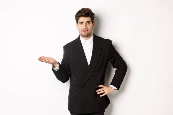 Image of confused handsome man in formal suit, raising hand and shrugging, cant understand something, standing against white background — Stock Photo, Image