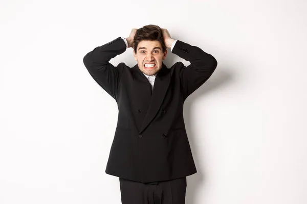 Imagen de hombre de negocios frustrado y enojado en traje negro, rasgando pelo en la cabeza y enloqueciendo, de pie tenso sobre fondo blanco — Foto de Stock