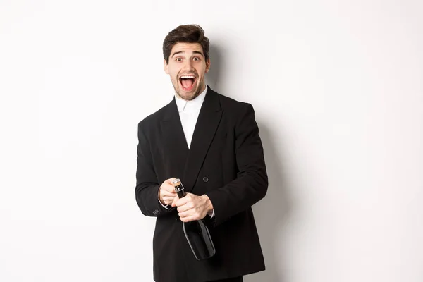 Bild av attraktiv man i svart kostym att ha en fest, fira nyår och öppna flaska champagne, stående glad mot vit bakgrund — Stockfoto