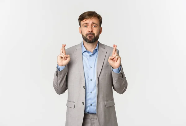 Retrato de homem de negócios triste esperançoso orando e fazendo desejo, cruzando os dedos para boa sorte, olhando preocupado com a câmera, de pé sobre fundo branco — Fotografia de Stock