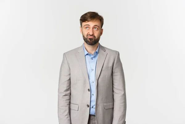 Porträt eines skeptischen und aufgebrachten bärtigen Büroangestellten im grauen Anzug, der enttäuscht auf das Logo in der oberen linken Ecke blickt, das vor weißem Hintergrund steht — Stockfoto