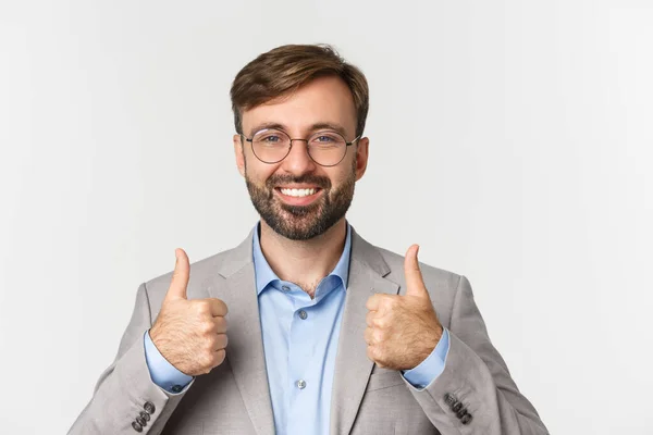 Close-up of handsome bearded man in glasses and gray suit, showing thumbs-up approval, like something, recommend product or brand, standing over white background — Stock Photo, Image