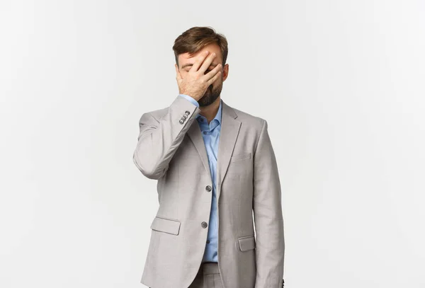 Retrato de homem de negócios cansado e irritado barbudo em terno cinza, facepalming, tapa o rosto e de pé angustiado sobre fundo branco — Fotografia de Stock