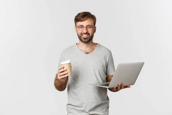 Portret van knappe mannelijke freelancer, koffie drinken en werken met laptop, staande over witte achtergrond — Stockfoto