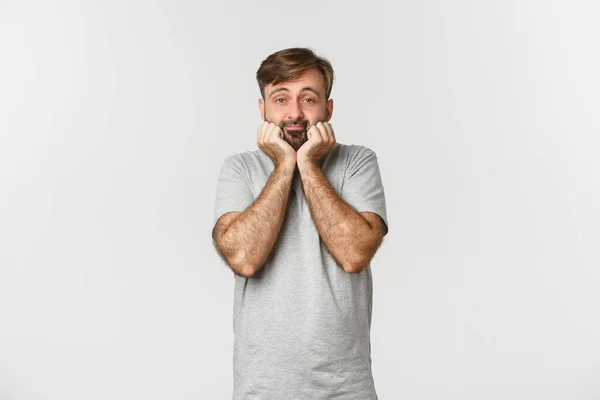 Portret van een leuke en domme volwassen man met baard, leunend op de palm en kijkend naar camera dom, staande over een witte achtergrond — Stockfoto