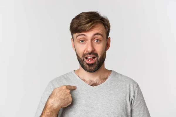 Close-up de homem bonito surpreso com barba, apontando para si mesmo e olhando confuso, de pé sobre fundo branco — Fotografia de Stock