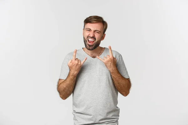 Portrét bezstarostného vousatého muže, jak se baví, ukazuje rock-n-rollové gesto a křičí radostí, stojí nad bílým pozadím — Stock fotografie