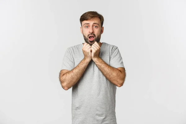 Portret van een barmhartige man met baard, draagt een grijs t-shirt, hijgend en bezorgd kijkend, staand over een witte achtergrond — Stockfoto