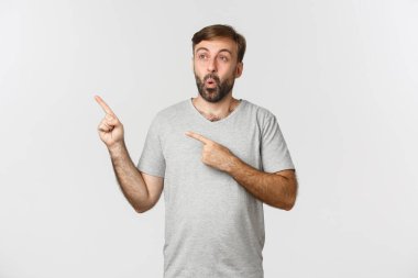 Gri tişörtlü yakışıklı adam, sol üst köşede mutlu ve etkilenmiş görünüyor, logoyu gösteriyor, beyaz arka planda duruyor.