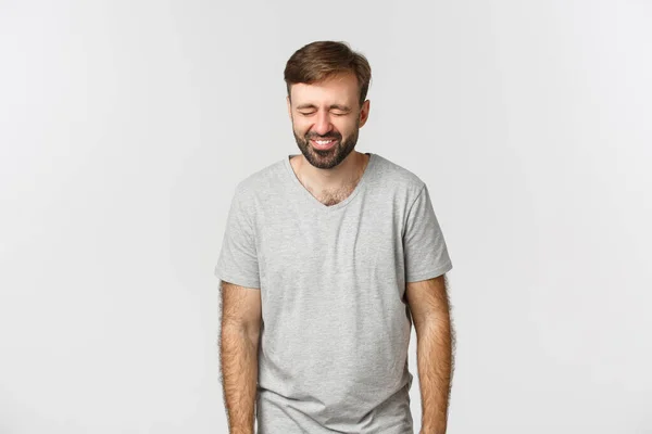 Imagem de cara barbudo alegre em camiseta cinza, rindo e se divertindo, de pé sobre fundo branco — Fotografia de Stock