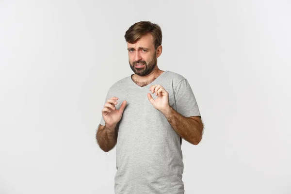 Portret van een timide en bange man in een grijs t-shirt, handen opsteken om zich te verdedigen, bang kijken, over een witte achtergrond staan — Stockfoto