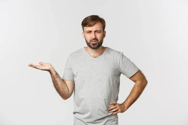 Портрет смущенного и раздраженного парня спорящего, поднимающего руку и выглядящего озадаченным, стоящего на белом фоне — стоковое фото