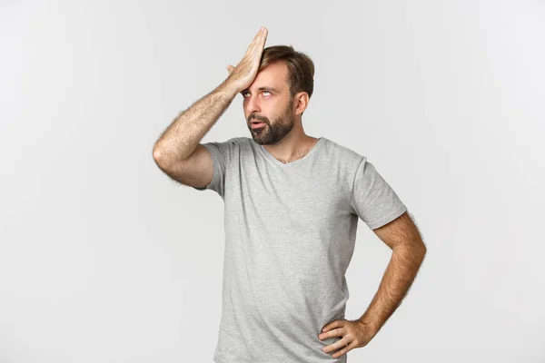 Afbeelding van geïrriteerde man in grijs t-shirt, klap voorhoofd en rollende ogen geïrriteerd, staande over witte achtergrond — Stockfoto