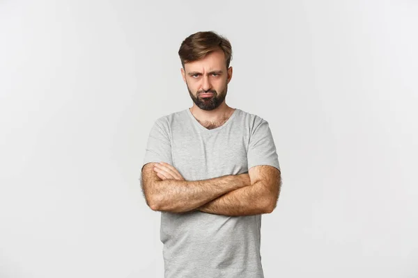 Portret van een beledigde knappe man, mokkend en boze grimas makend, handen over de borst defensief, staand over een witte achtergrond — Stockfoto