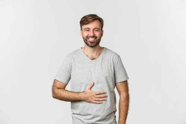 Retrato de homem feliz sentindo-se satisfeito depois de comer comida saborosa, esfregando barriga e sorrindo encantado, de pé sobre fundo branco — Fotografia de Stock