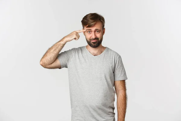 Retrato de cara frustrado repreendendo alguém por ser louco ou estranho, apontando para a cabeça e franzindo a testa, de pé sobre fundo branco — Fotografia de Stock