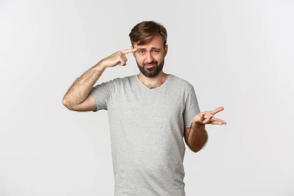 Portret van een gefrustreerde man die iemand uitschold omdat hij gek of vreemd was, naar zijn hoofd wees en fronste, over een witte achtergrond stond — Stockfoto