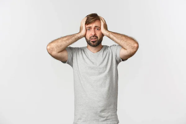 Porträtt av oroliga man som har panik, hålla händerna på huvudet och står alarmerade över vit bakgrund — Stockfoto