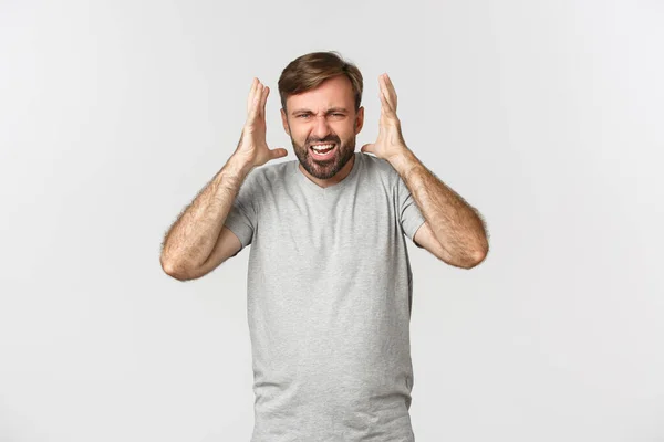 Retrato de homem barbudo com raiva, gritando e apertando as mãos frustrado, de pé louco sobre fundo branco — Fotografia de Stock