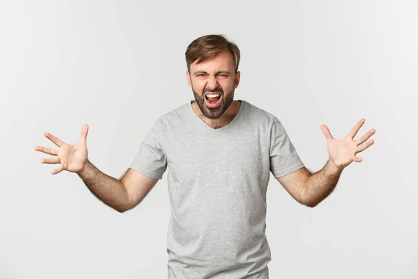 Retrato de homem barbudo com raiva, gritando e apertando as mãos frustrado, de pé louco sobre fundo branco — Fotografia de Stock