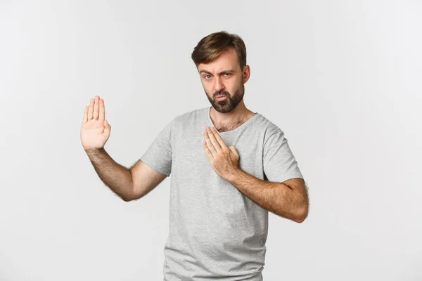 Homem barbudo engraçado em camiseta cinza, mostrando habilidades de artes marciais e amuado, de pé sobre fundo branco — Fotografia de Stock