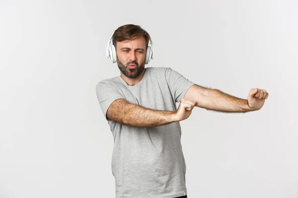 Portrait of happy guy dancing to music in headphones, standing over white background — Stock Photo, Image
