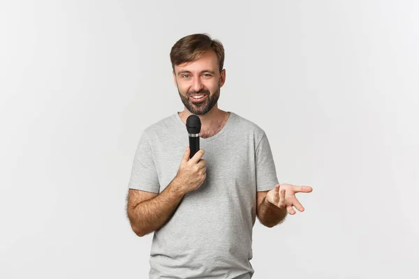 Image of charismatic man in gray t-shirt making a speech, holding microphone and talking, standing over white background — Stock Photo, Image