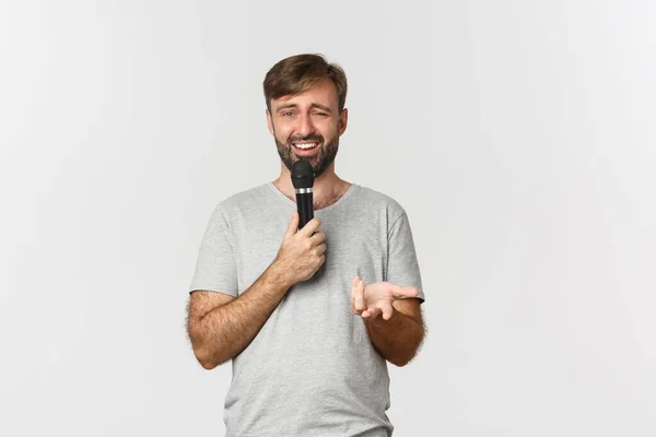 Imagem de cara com barba, vestindo camiseta cinza, fazendo discurso com microfone e olhando confuso, em pé sobre fundo branco — Fotografia de Stock