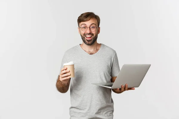 Portret van knappe mannelijke freelancer, koffie drinken en werken met laptop, staande over witte achtergrond — Stockfoto