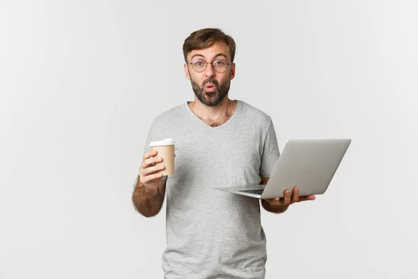 Portret van een knappe mannelijke freelancer, koffie drinken en werken met een laptop, verrast kijken, over een witte achtergrond staan — Stockfoto