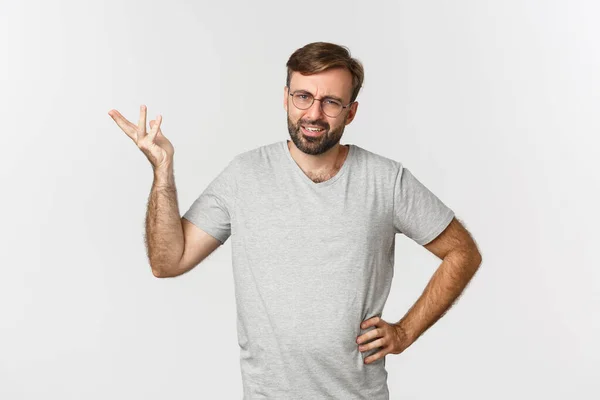 Portret van een knappe volwassen man die er verward uitziet, hand omhoog steekt en verbijsterd kijkt, over een witte achtergrond staat — Stockfoto