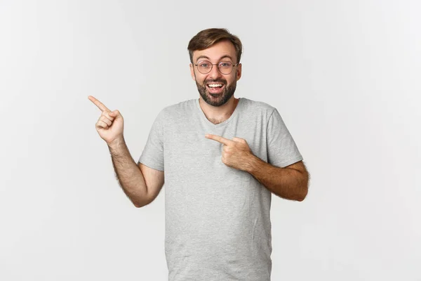 Excited bearded man smiling, pointing fingers at upper left corner, showing logo, standing over white background — Stock Photo, Image