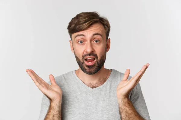 Primer plano del hombre guapo sorprendido con barba, las manos extendidas hacia los lados y mirar con asombro, de pie sobre el fondo blanco — Foto de Stock