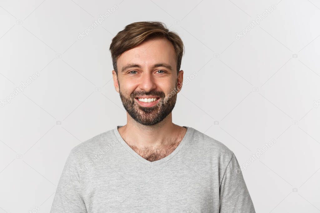 Close-up of handsome adult man with beard, wearing gray t-shirt, smiling happy, standing over white background