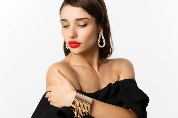 Concepto de moda y belleza. Mujer elegante con labios rojos, vestido negro, mostrando pendientes y joyas, fondo blanco — Foto de Stock