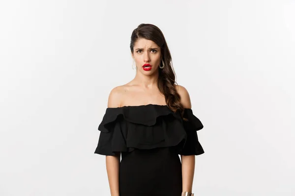 Moda e beleza. Mulher decepcionada e chateada em vestido preto olhando para a câmera descontente, reclamando com olhar ciumento, em pé sobre fundo branco — Fotografia de Stock