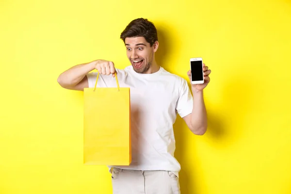 Boldog ember nézi bevásárló táska és mutatja a mobiltelefon képernyőn. Az online banki szolgáltatások és a pénz fogalma — Stock Fotó