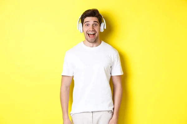 Mann mit Kopfhörer sieht überrascht aus, steht im weißen Outfit vor gelbem Hintergrund — Stockfoto