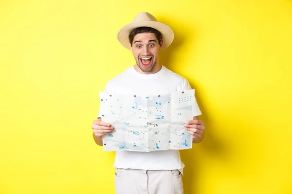 Concepto de viaje, vacaciones y turismo. Hombre turista mirando feliz en el mapa con vistas, explorar la ciudad, de pie sobre el fondo amarillo — Foto de Stock