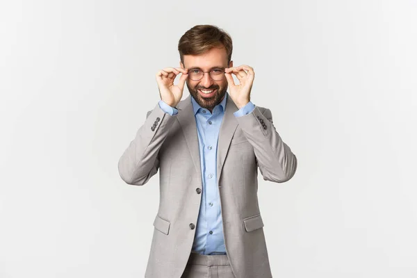 Muotokuva onnistunut parrakas liikemies harmaa puku, laittaa lasit ja hymyillen tyytyväinen, seisoo valkoisella taustalla — kuvapankkivalokuva