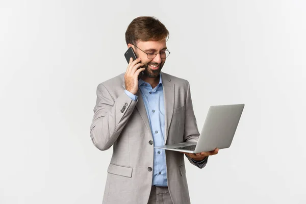 Beeld van succesvolle zakenman praten op de telefoon en op zoek tevreden op laptop scherm, werken over witte achtergrond — Stockfoto