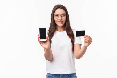 Heyecanlı ve baştan çıkarıcı genç bir kadının portresi alışverişi seviyor, yeni kredi kartını online mağazada kullanmak için sabırsızlanıyor, cep telefonu ekranını gösteriyor, banka hesabıyla övünüyor, dudaklarını ısırıyor.