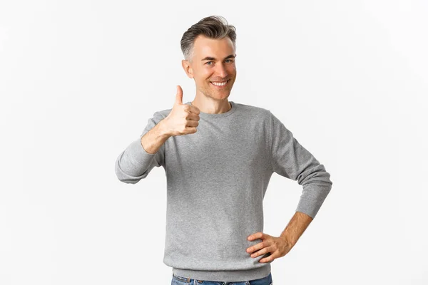 Портрет гордого и счастливого мужчины средних лет, улыбающегося довольного и показывающего большие пальцы вверх, восхваляющего что-то хорошее, стоящего на белом фоне — стоковое фото