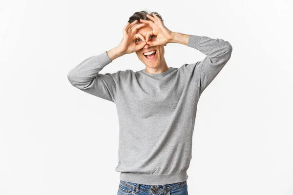 Portrait d'un homme drôle d'âge moyen faisant des visages, montrant des lunettes de main autour des yeux comme si on regardait à travers des jumelles, debout sur fond blanc — Photo