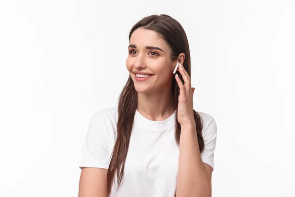 Közelkép portré vonzó mosolygós fiatal barna nő beszél telefonon, a vezeték nélküli fülhallgató, hogy vegye fel a kapcsolatot a barátjával, néz félre gondtalan, zenét hallgatni fülhallgató, fehér háttér — Stock Fotó