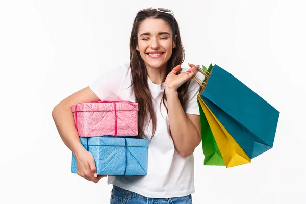 Shopping, holidays and lifestyle concept. Portrait of cheerful excited young woman smiling as likes making presents for friends, close eyes imaging how she give gifts, hold shop bags — Stock Photo, Image