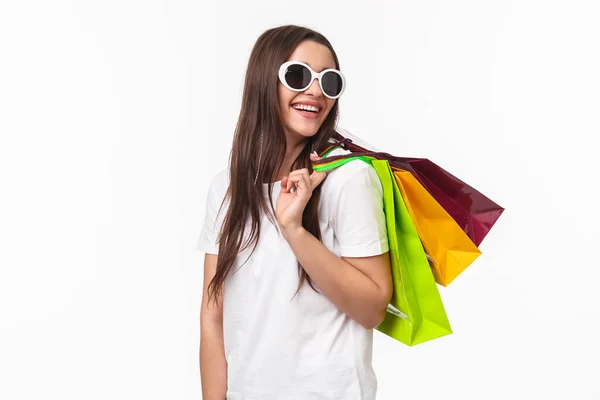 Shopping, leisure and lifestyle concept. Happy, joyful young feminine woman walking in store, buying new clothes and summer bikini, look back with smiling pleased look, hold bags on shoulder — Stock Photo, Image