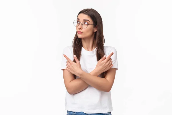 Retrato de cintura hacia arriba de una joven indecisa y reflexiva en gafas, estudiante de 20 años escogiendo su camino, señalando con los dedos hacia los lados izquierda y derecha, tomando decisiones, pensando en el fondo blanco — Foto de Stock